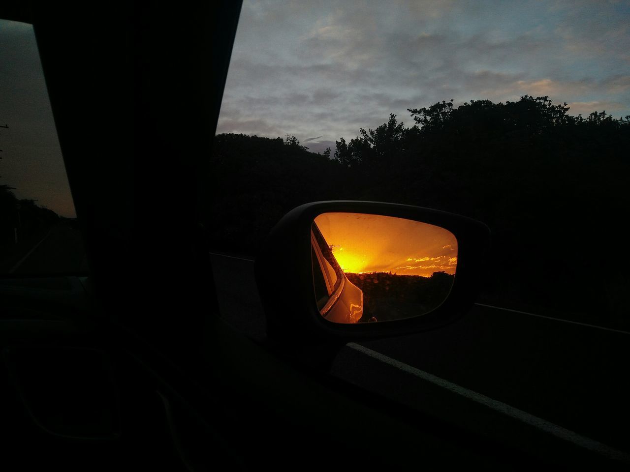 CAR ON SIDE-VIEW MIRROR AGAINST SUNSET SKY