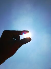 Close-up of hand holding sun shining through blue sky