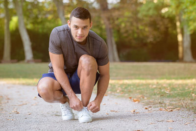 Young man looking away while sitting on tree