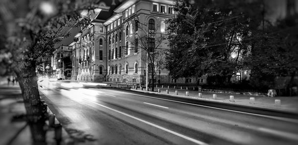 Illuminated street by buildings in city at night