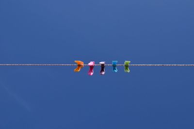 Low angle view of clothespins on rope against clear blue sky