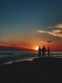 Silhouette men standing on beach against sky during sunset