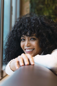 Smiling curly haired woman leaning on sofa at cafe