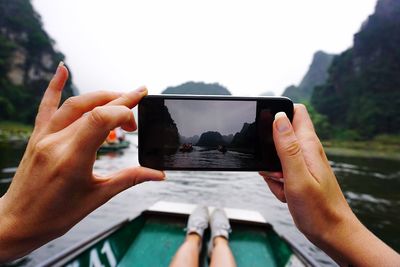 Cropped image of woman photographing sea through smart phone while sitting on boat