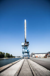Crane by pier against clear blue sky