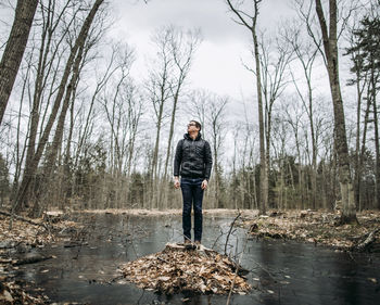 Tall man stands on stump in middle of swamp on cold cloudy day