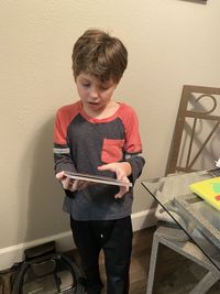 Boy holding book while standing at home