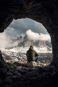 Rear view of man sitting on rock looking at mountains
