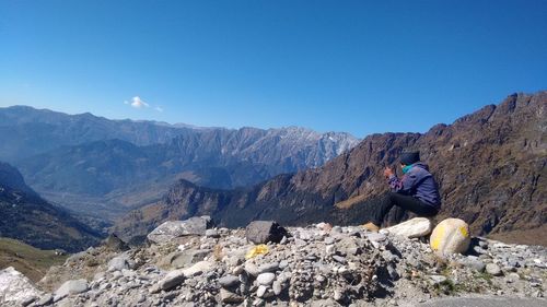 Side view of male hiker sitting on cliff against mountains