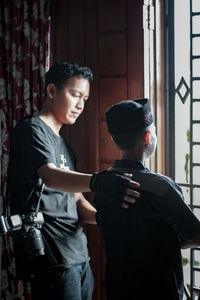 Young man holding camera while standing at home