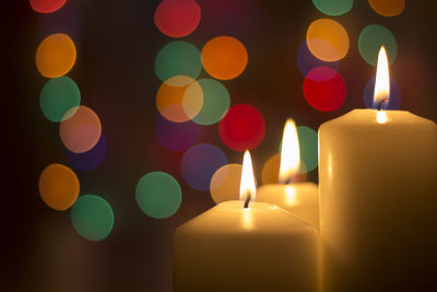 Close-up of candles burning against illuminated christmas lights in darkroom