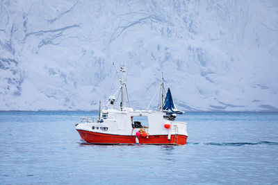 Boat sailing in sea by snowcapped mountain