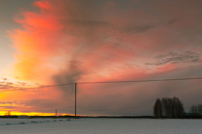 Field covered with snow against cloudy sky during sunset