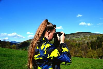 Side view of woman photographing on field against sky