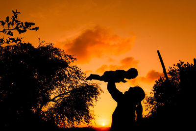 Silhouette people by tree against orange sky