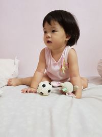 Cute baby girl with toys sitting on bed against wall at home