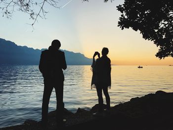 Silhouette friends standing on sea against sky during sunset