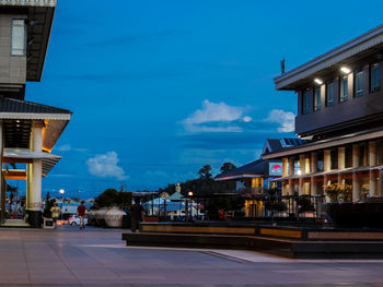 Illuminated buildings by road against blue sky