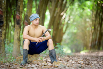 Full length of thoughtful shirtless man sitting in forest