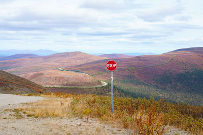 Red road sign on land against sky