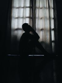 Silhouette woman looking through window at home