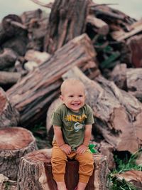 Portrait of smiling boy sitting on tree trunk