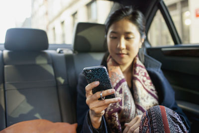 Young asian businesswoman looking at smartphone sitting in car service limousine