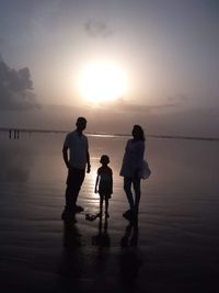 People standing on beach against sky during sunset