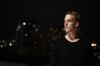 Portrait of young man standing against illuminated city at night