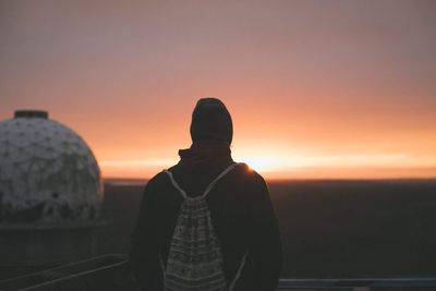 Rear view of silhouette young man with backpack standing against sky during sunset