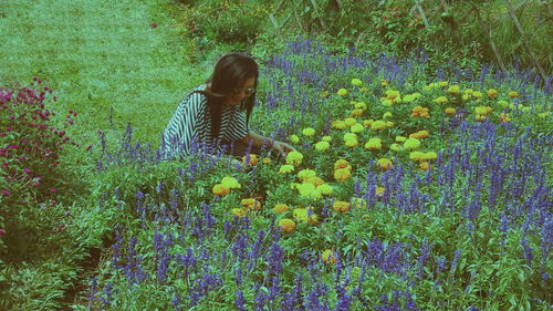 Smiling woman crouching by flowers blooming on field