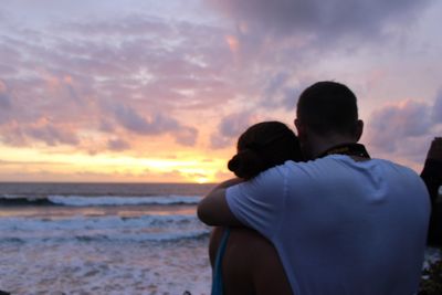 Rear view of couple on beach against sky during sunset