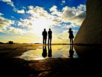 Silhouette people standing on footpath against sky during sunset