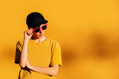 Young man wearing sunglasses standing against yellow wall