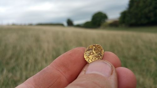 Close-up of hand holding old weathered golden coin on land