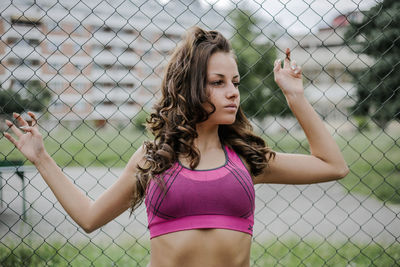 Young woman looking away while standing by chainlink fence