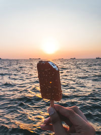 Cropped hand of woman holding sea against sky during sunset