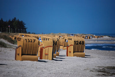 Hooded chairs on beach against clear blue sky