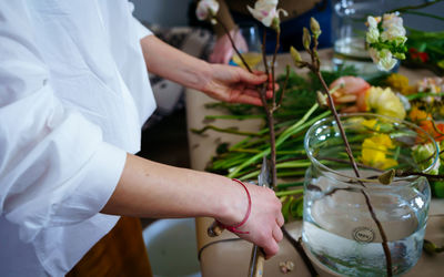 Women hands make bouquet at flower workshop with magnolia branches