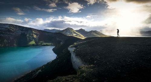 Silhouette man standing on mountain against cloudy sky during sunset