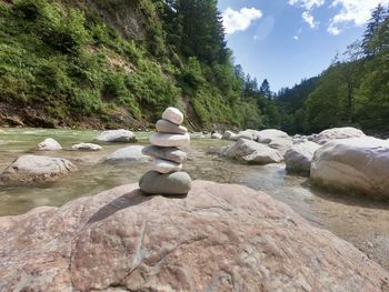 Stack of stones on rock by trees against sky