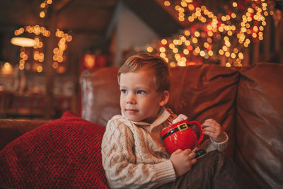 Portrait candid happy kid in knit beige sweater hold xmas mug with marshmallows and candy cane