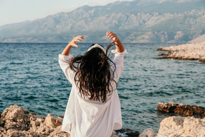 Rear view of young woman in white shirt on beach. long hair, hairstyle, lifestyle.