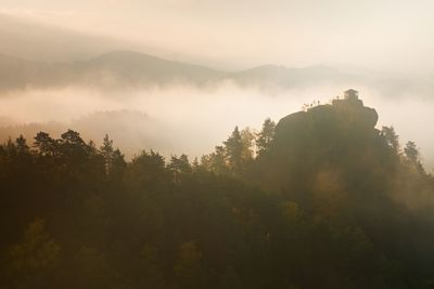 Misty daybreak in a valley of bohemian switzerland park. hill with hut on hill in magical darkness.