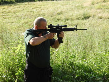 Senior man using rifle while standing on field