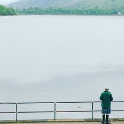 Rear view of man standing by railing against sky