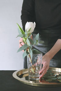 Midsection of person holding flower vase on table