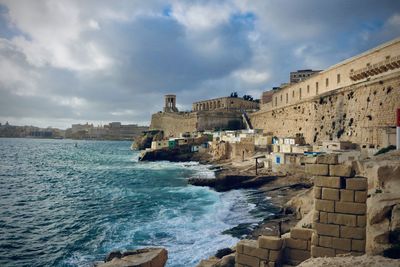 Buildings by sea against cloudy sky