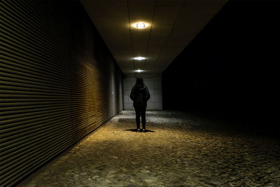 Rear view of man walking in illuminated corridor