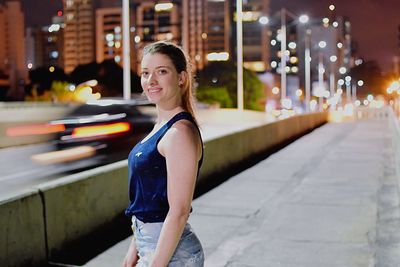 Portrait of smiling young woman standing in city at night